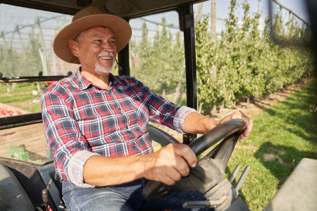 Senior farmer driving a tractor through apple orchardの写真素材