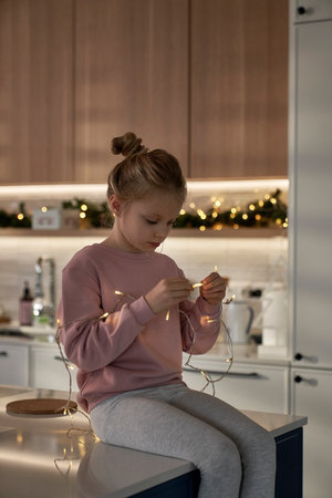 Caucasian girl playing with Christmas lights in the kitchenの写真素材