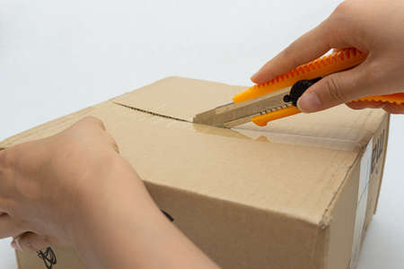 Unboxing the courier box with a cutter knifeの写真素材