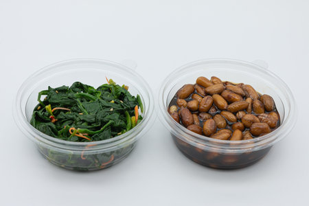 Stir-fried spinach and beans in plastic container on white backgroundの写真素材