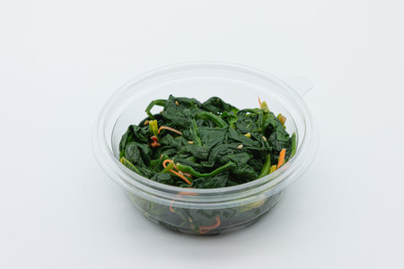 stir-fried spinach in a plastic container on a white backgroundの写真素材