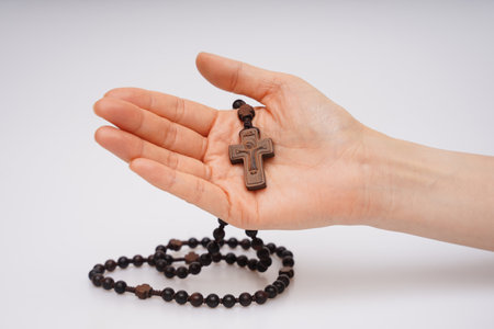Wooden rosary with a cross in hand on a white backgroundの写真素材