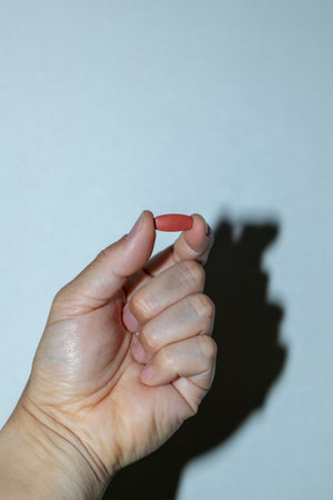 Female hand holding a red pill in front of a white background.の写真素材