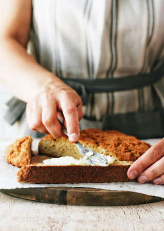 Person in an apron buttering a slice of homemade bread.