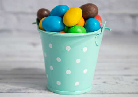 Colorful candies lie in a small decorative mint color bucket. Close-up miniatures on a white brick background.の写真素材