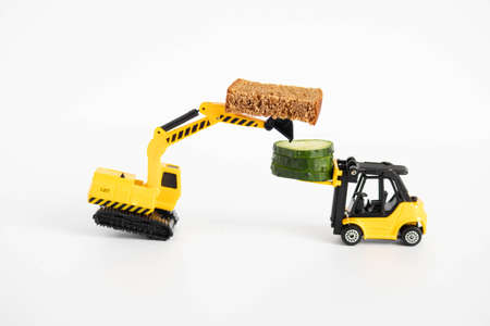 A toy loader or construction crane in bright yellow carries a piece of cucumber and a piece of black...