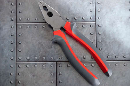 Construction tool pliers with red handles lie on a gray iron background.
