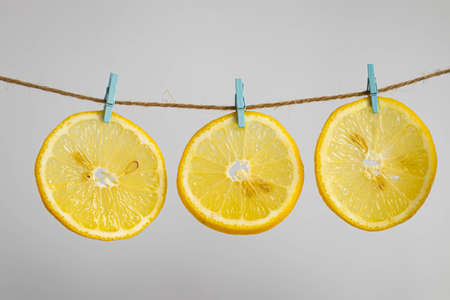Three round slices of bright yellow juicy lemon hang on jute on wooden clothespins. As if clothes...