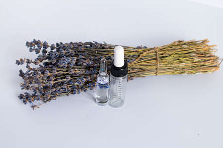 Bouquet of dried lavender flowers on a white background. Lavender essential oil. A transparent glass...