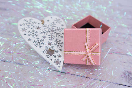 Pink gift box with a gold bow on a sparkling background. Gift wrapping for a holiday. Nearby lies a white openwork heart made of wooden materialの写真素材