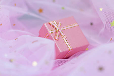 Pink gift box with golden bow lies on sparkling background. Gift wrapping for a holiday.の写真素材
