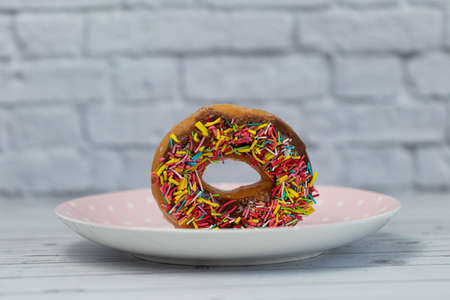 Pastries concept. Donuts with chocolate glaze with colorfull sprinkles, on a pink plate. side viewの写真素材