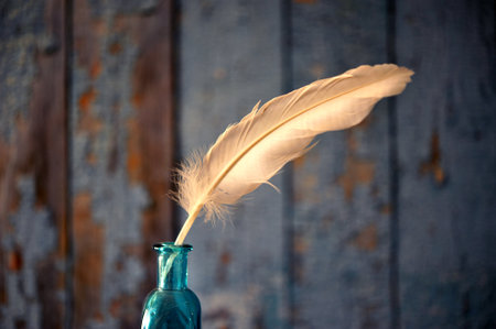 White feather in turquoise bottle against wall with flaky blue paint. Closeup with copy space.の写真素材