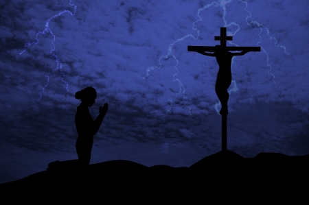 Silhouette of a woman praying under the crossの写真素材