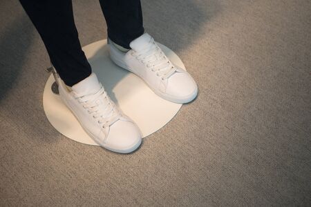 Window display of a male mannequin wearing white shoes.