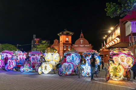 Malacca,Malaysia - September 20,2024 : A row of rickshaws decorated with colourful lighting parking in front of the Dutch Square at night, people can seen exploringのeditorial素材