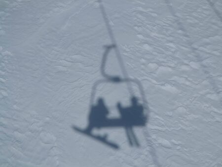 Shadows of a snowboarder and skier riding a chair liftの写真素材