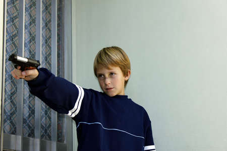 Juvenile delinquency. Beaten child pointing at the door of a house with a gunの写真素材