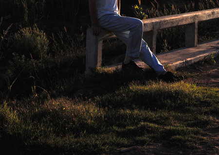 Young man sitting on a bench in a park at sunset in summer