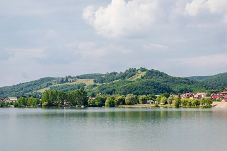 Wide view of a large lake with trees houses and forest covered hill in the backgroundの写真素材