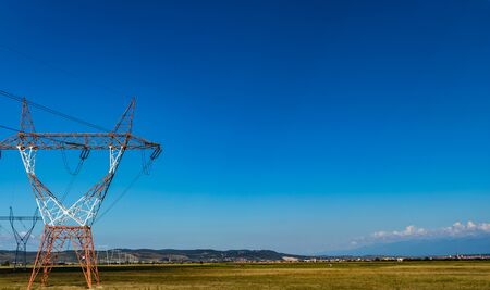 High voltage power lines on power pylons on a large grass fieldの写真素材