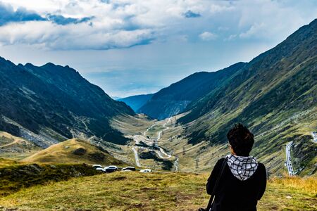 Woman gazing upon cars on a curvy mountain road passing through a mountain valleyの写真素材