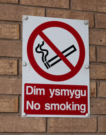 Bilingual no smoking sign in English and Welsh on an exterior brick wall Wrexham Wales June 2018の写真素材
