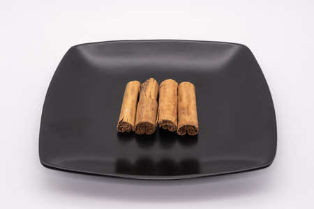 Cinnamon sticks on a square black plate against a white backgroundの写真素材