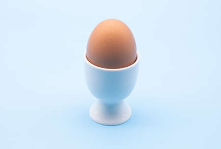 egg in a white cup isolated against a light blue backgroundの写真素材