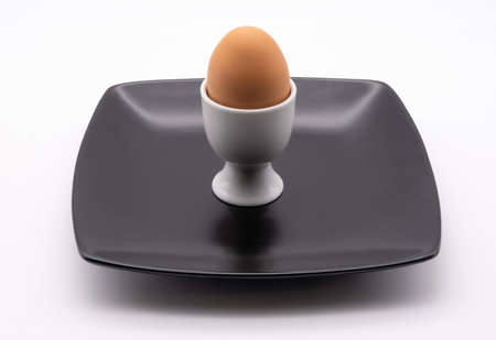 egg in a white cup on a black plate against a plain white backgroundの写真素材