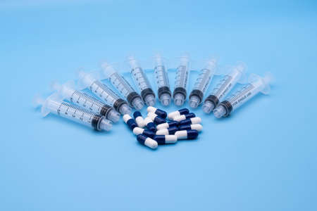 multiple clear plastic 5ml syringes with blue and white capsule tablets isolated against a light blue backgroundの写真素材