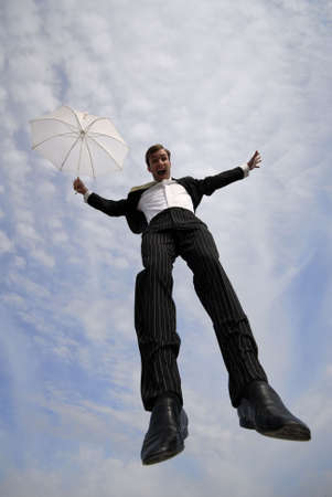 businessman jumps with  umbrella on  background of  blue sky with cloudsの写真素材