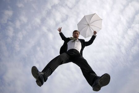 businessman jumps with  umbrella on  background of  blue sky with cloudsの写真素材