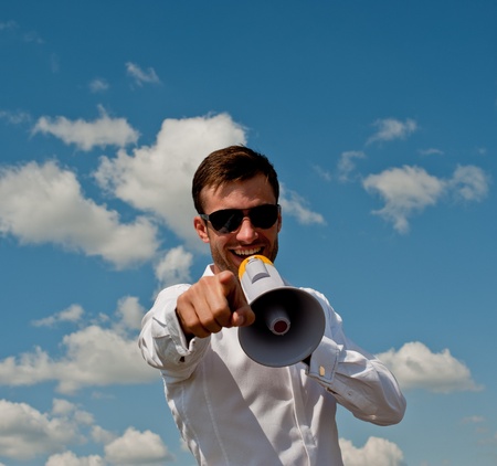nice young businessman shouts in a megaphone against the blue sky with cloudsの写真素材