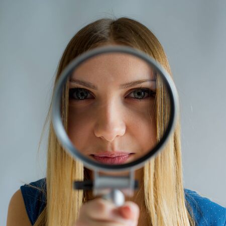 beautiful woman with magnifying glass in hands looks in a camera lens