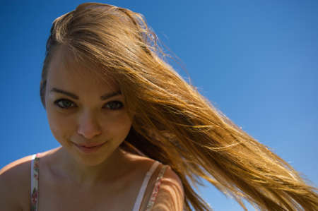 portrait of the smiling girl with a flowing hair against the blue skyの写真素材