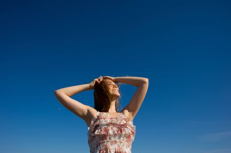 girl with the raised hands looks aside against the blue skyの写真素材