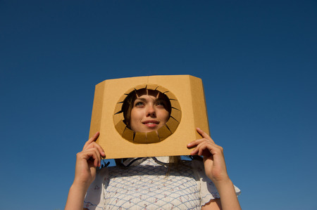 woman looks through a cutout in the paper on the background of blue skyの写真素材