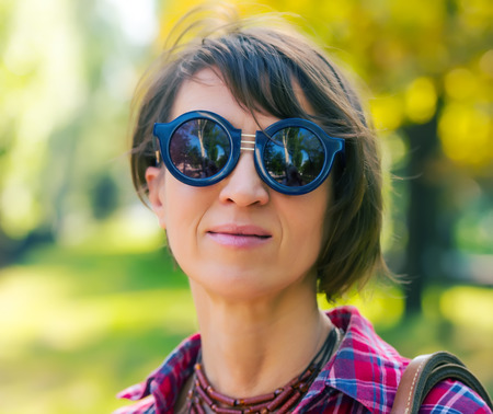 portrait of a pretty woman in sunglasses on background of city park, age forty to forty-five years の写真素材