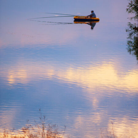 fisherman in a boat and sky reflection in the lake, evening