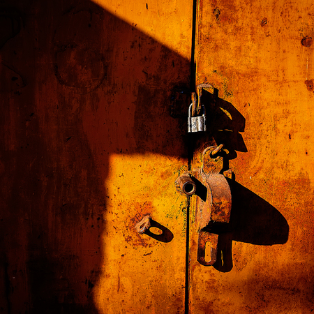 manual lock hangs on a rusty metal door closedの写真素材