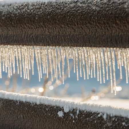 wooden fence covered with snow and ice in sunny dayの写真素材