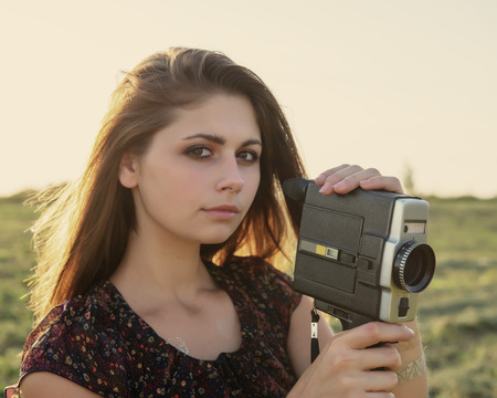 girl with a cinema camera on a meadow at sunset