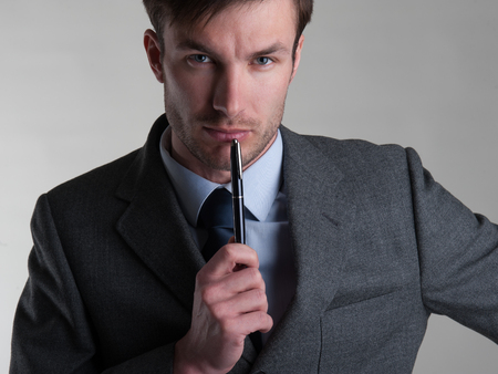 Friendly businessman with pen in hand looks at cameraの写真素材