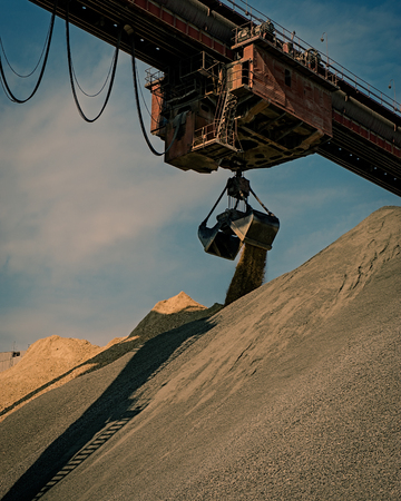 Industrial crane works on loading a mixture of sand and gravel