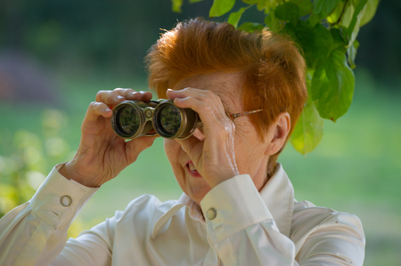 Aged woman looking through binoculars in a park. Age eighty years.の写真素材