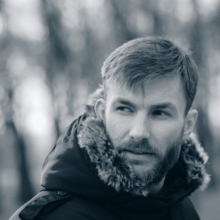 Man With A Beard Corrects His Hood And Looks Away On A Blurred Background Of Trees. Portrait Man. Bearded Man.の写真素材