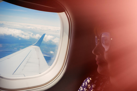 female passenger is sitting by the airplane window. The wing of the plane. Clouds and the surface of the earth.の写真素材