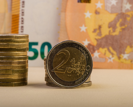 coin of two euros and a stack of folded coins against a background of a faded paper bill of fifty euros. Euro money.  Currency of the European Union.の写真素材