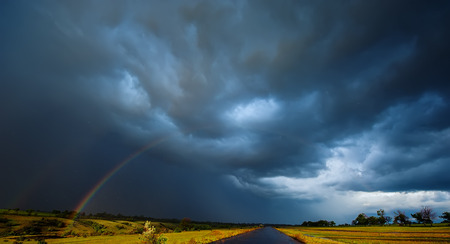 rainbow in the field rain and dark clouds. Spring season, evening. Panoramic and web banner.の写真素材